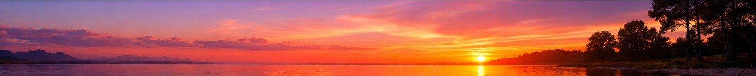 Sunset over water with trees and distant clouded mountains